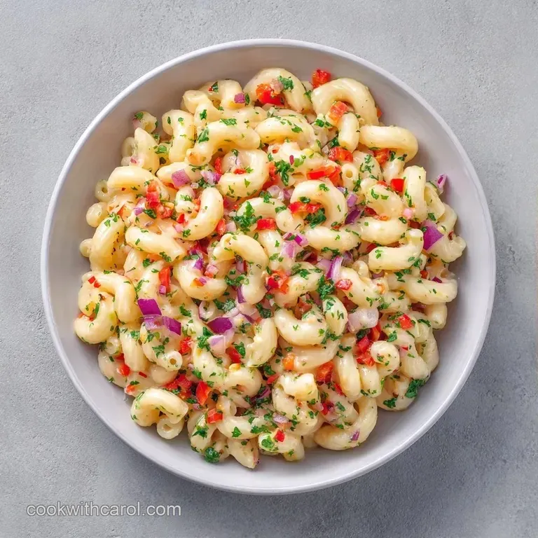 A chilled scoop of creamy pasta salad in a white ceramic bowl, topped with grated cheese and a sprig of fresh herb.